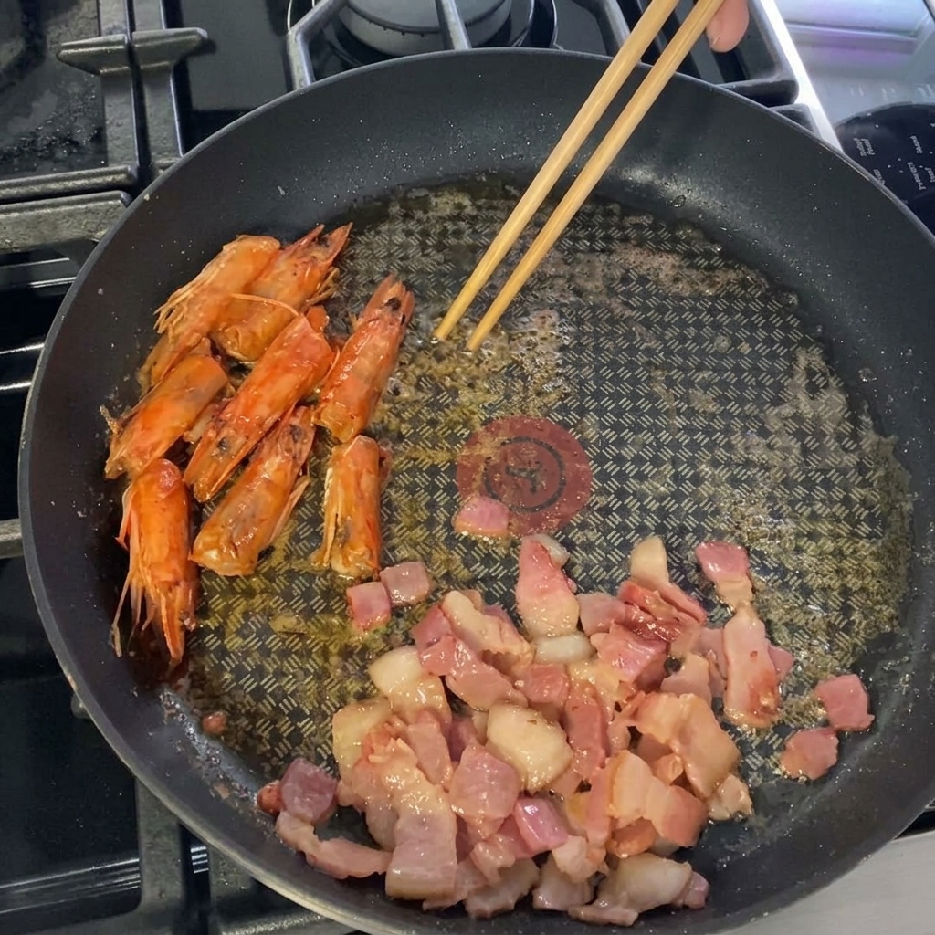 베이컨과 새우 머리가 있는 팬에 손질한 새우 살을 넣는 모습.