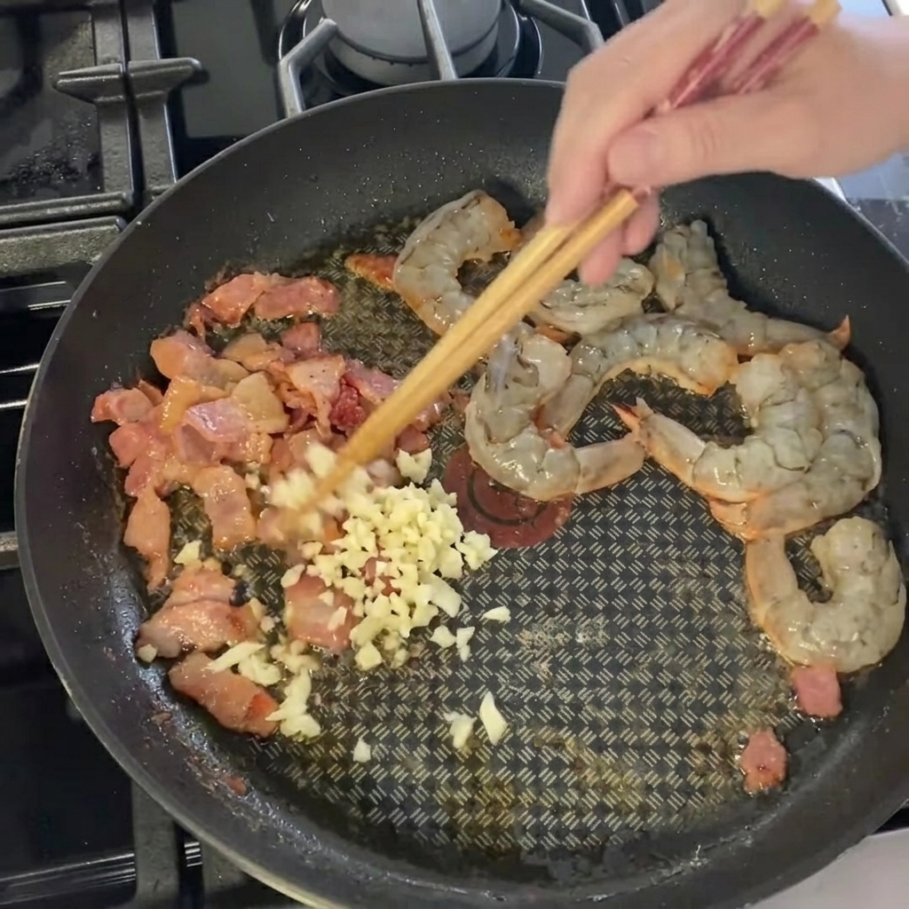 팬 속의 새우와 베이컨 위로 다진 마늘을 넣는 모습.