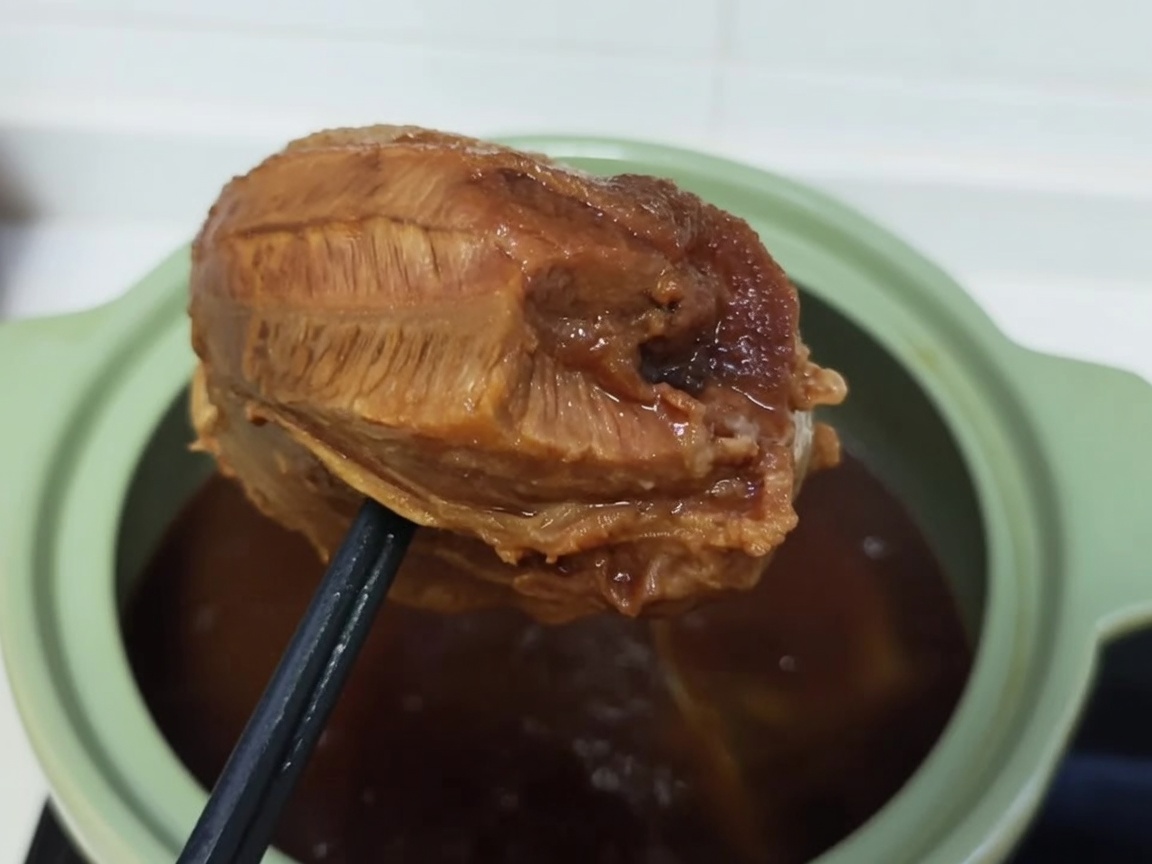 갈색으로 잘 익은 소고기 사태를 투명한 비닐 랩으로 단단히 감싸는 모습.