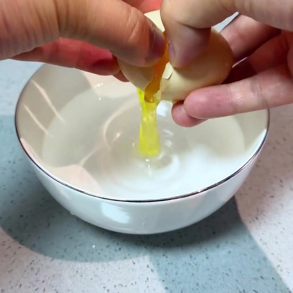 투명한 물이 담긴 작은 흰색 그릇에 조심스럽게 달걀을 깨 넣는 두 손.