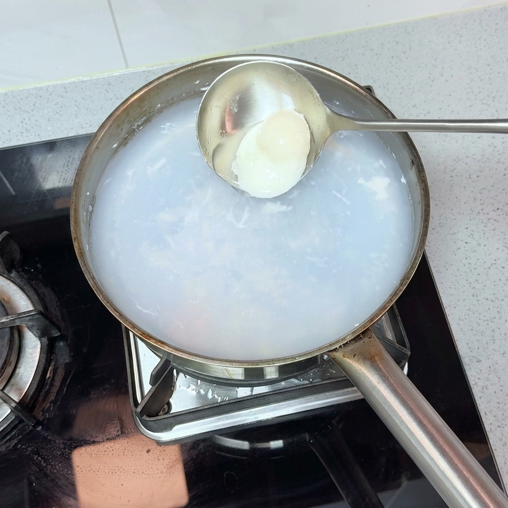 금속 국자로 뜨거운 물에서 수란을 조심스럽게 건져내는 모습.