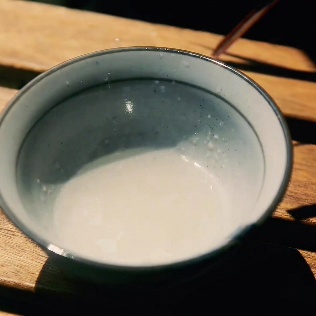 사케, 설탕, 간장이 섞인 나무 테이블 위의 작은 도자기 그릇.