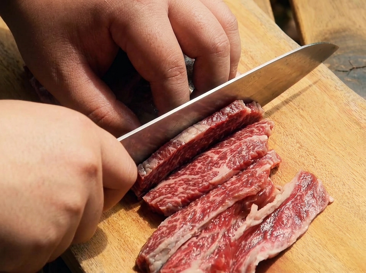 나무 도마 위에서 날카로운 칼로 생소갈비살을 얇게 써는 모습.