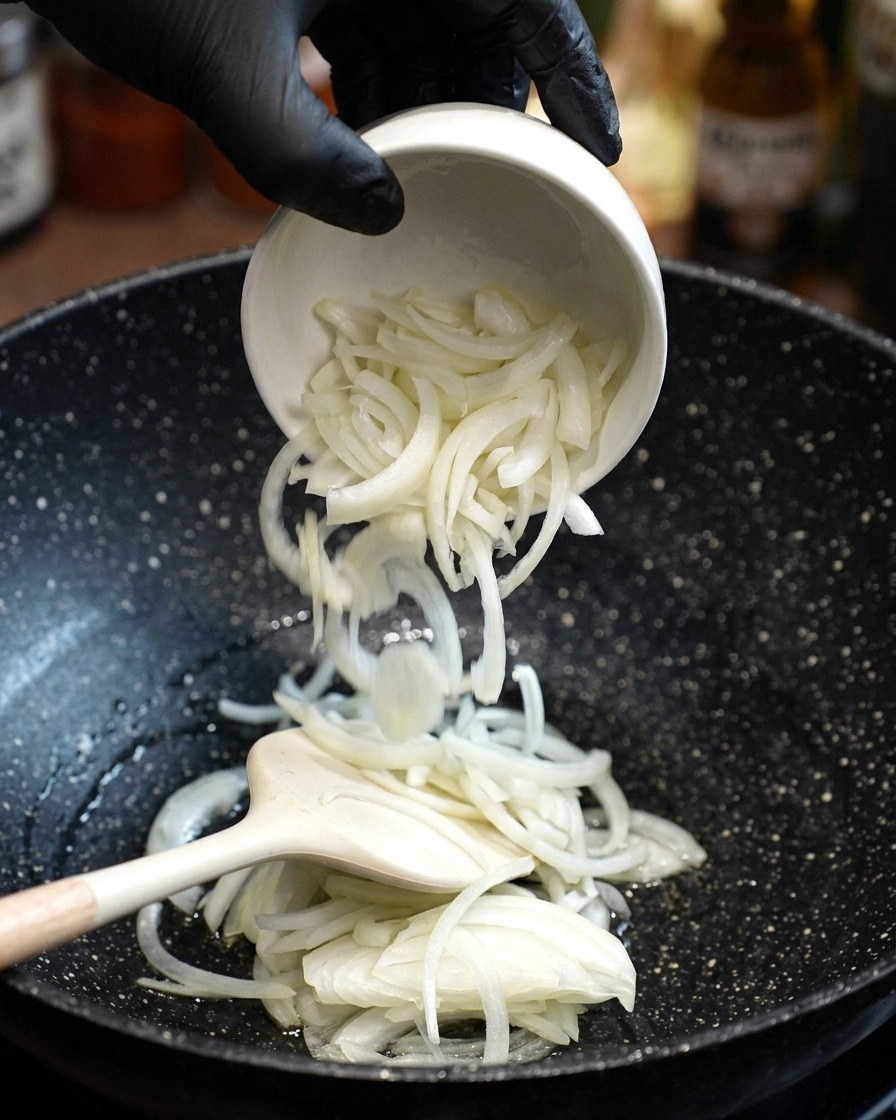 뜨거운 기름에 채 썬 양파를 넣고 뒤집개로 볶는 모습.