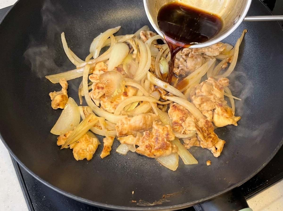 부드러워진 양파와 닭고기가 담긴 팬에 부어지는 어두운 소스.