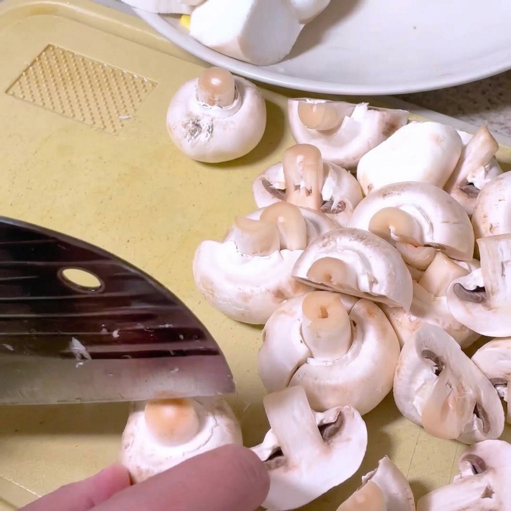 도마 위에서 주방 칼로 양송이버섯을 반으로 자르는 모습.