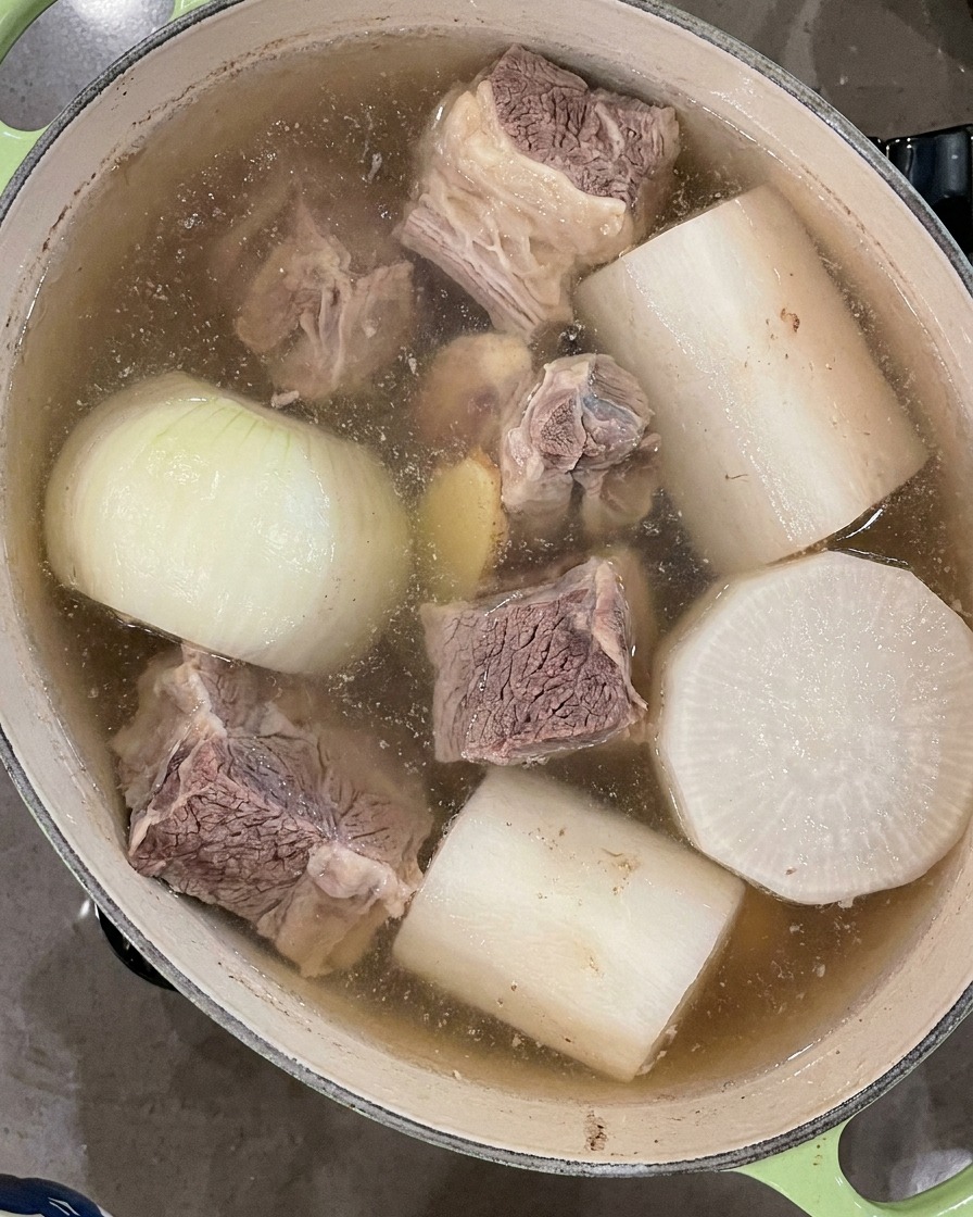 끓어오르는 국물 표면에 뜬 거품을 검은색 국자로 걷어내는 모습.