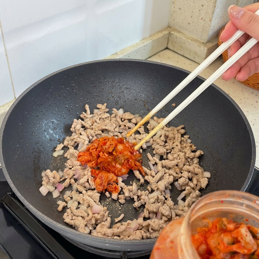 볶은 고기와 샬롯이 든 팬에 김치를 넣는 모습.