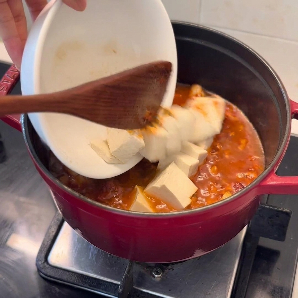 끓는 김치찌개에 두부 큐브를 조심스럽게 넣는 모습.