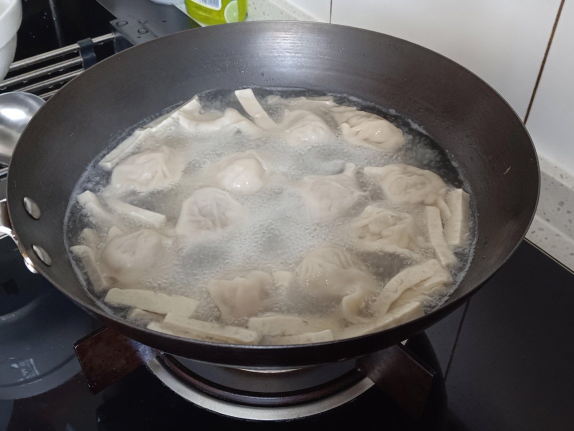 만두와 두부가 끓고 있는 냄비에 당면을 넣는 클로즈업 모습.