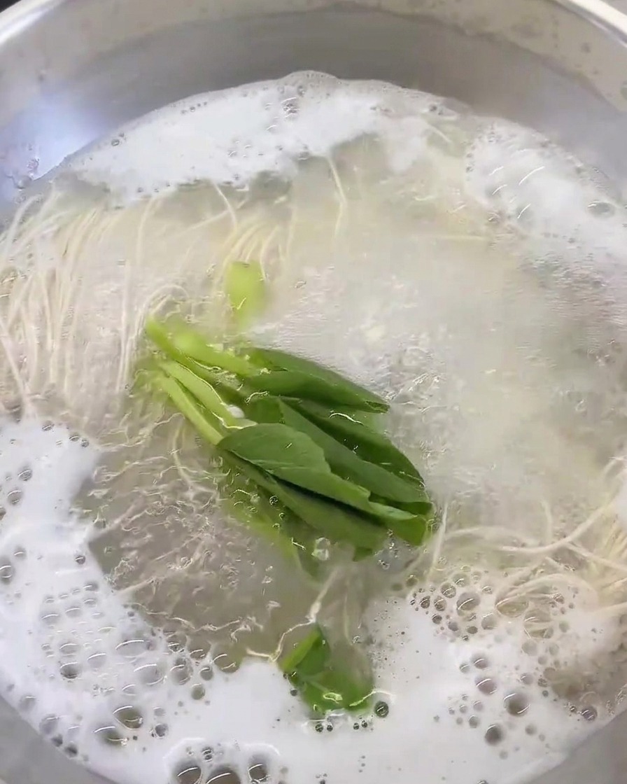 끓는 육수와 면이 담긴 냄비에 신선한 잎채소를 넣는 모습.