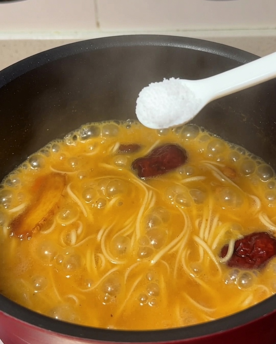 끓고 있는 면과 닭고기 수프가 담긴 냄비에 소금 한 숟가락을 넣는 모습.