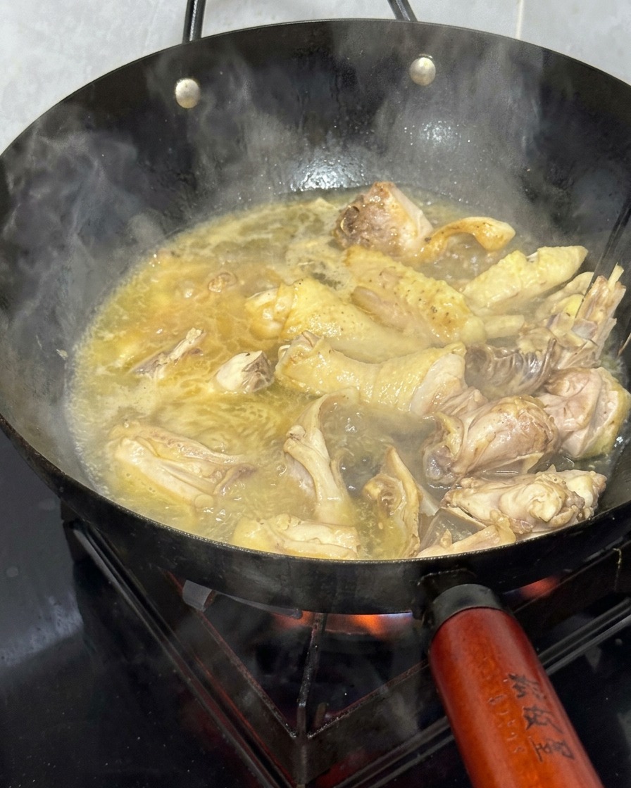 황금빛으로 끓어오르는 국물에 닭고기 조각이 담긴 웍.