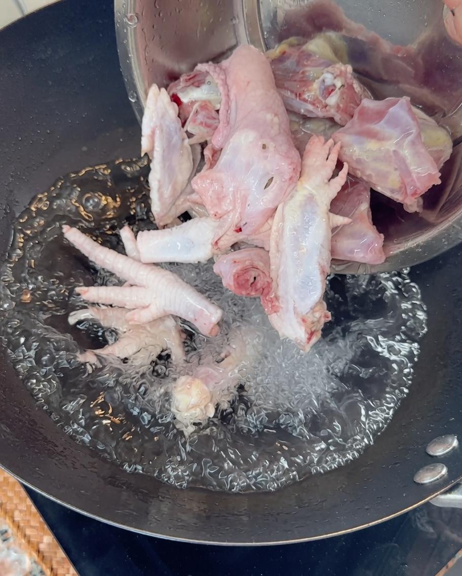 끓는 물이 담긴 웍에 닭 뼈와 발을 넣는 모습.