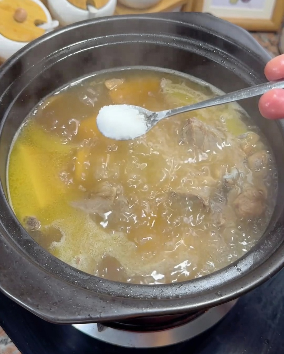 끓고 있는 황금빛 닭 육수에 소금을 넣는 모습.