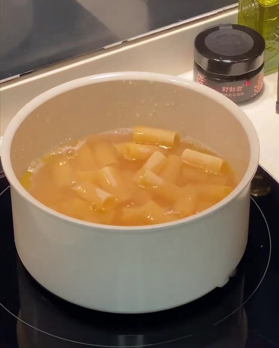 끓는 물에 리가토니 파스타가 삶아지고 있으며 표면에 기포와 기름 방울이 보입니다.