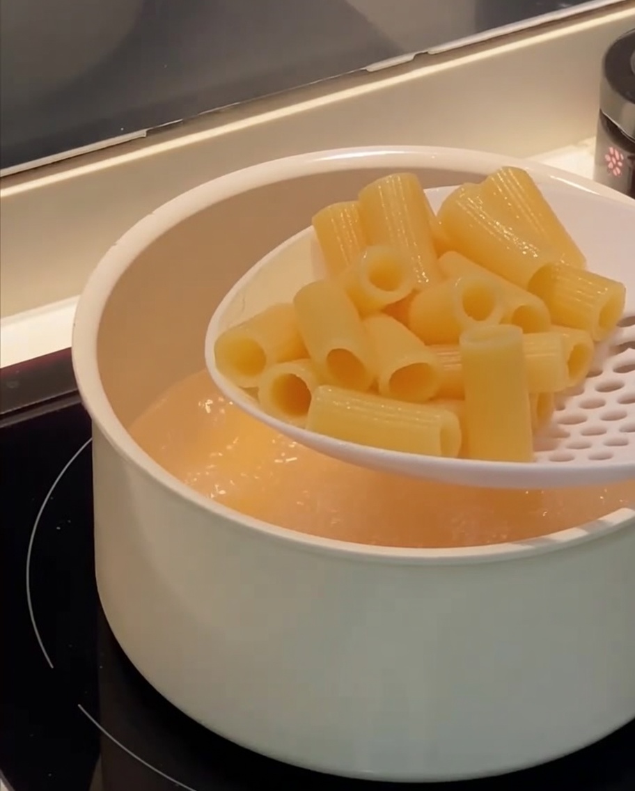 거품기로 삶아진 리가토니 파스타를 끓는 물에서 건져내는 모습.
