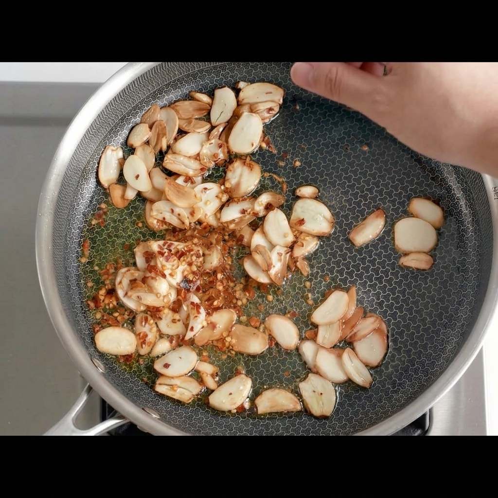 노릇한 마늘이 든 팬에 말린 고추 조각을 넣는 모습.