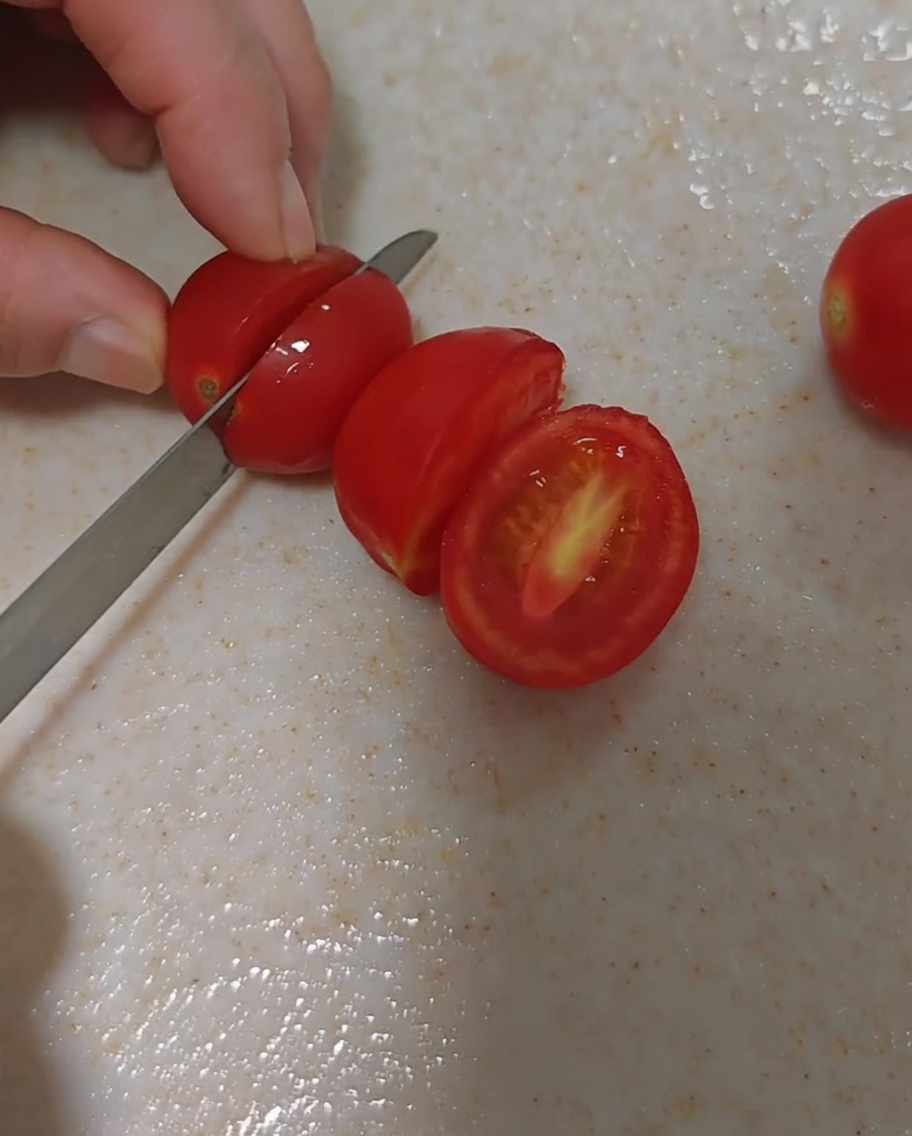 도마 위에서 조심스럽게 반으로 썰고 있는 신선한 방울토마토.