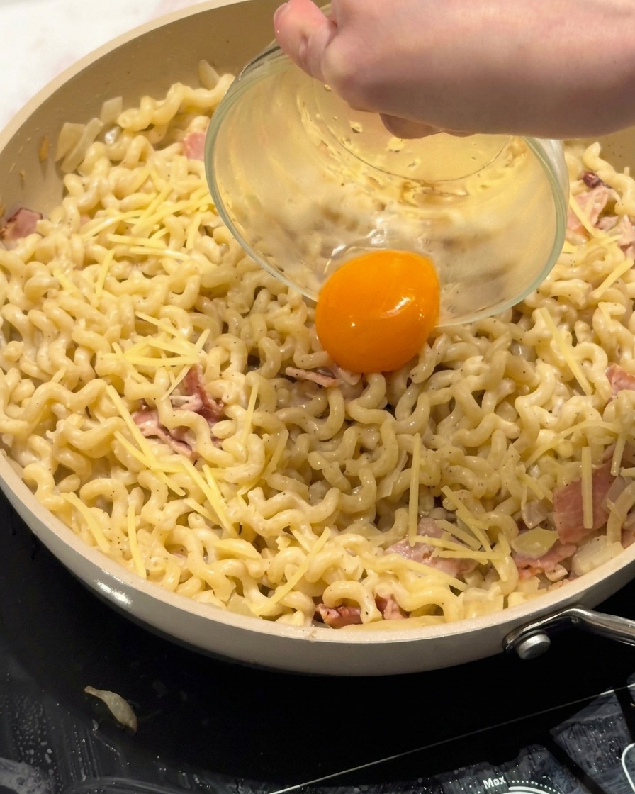 크리미한 파스타 중앙에 신선한 달걀노른자를 올리는 모습.