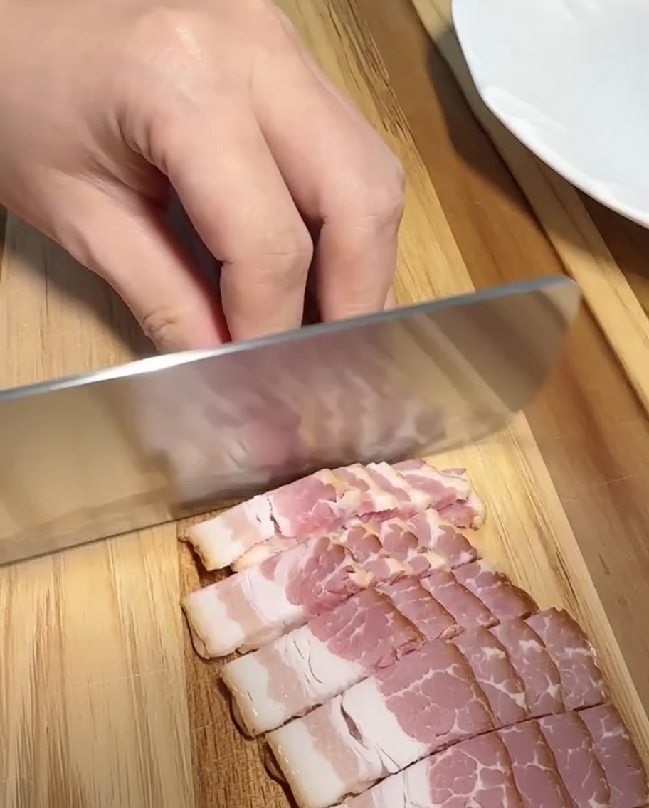 도마 위에서 베이컨을 작고 일정한 크기로 썰고 있는 모습.