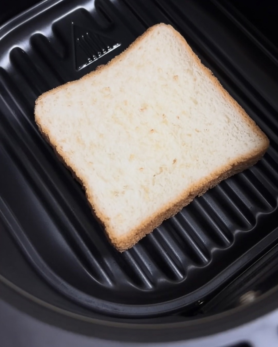 에어프라이어 바스켓 바닥에 평평하게 놓인 식빵 한 조각.