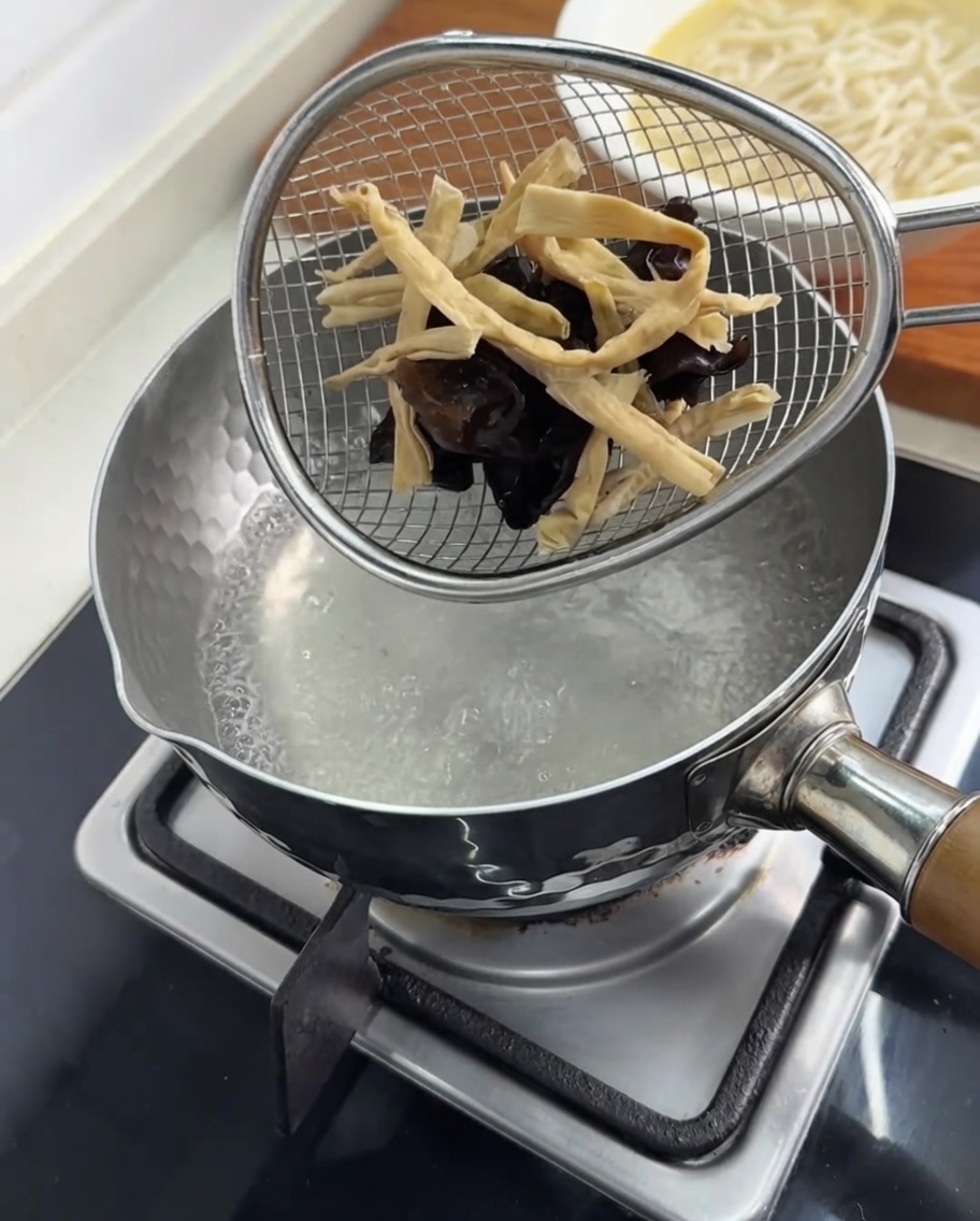 끓는 물이 든 냄비 안에서 채반에 담긴 목이버섯과 죽순을 데치는 모습.