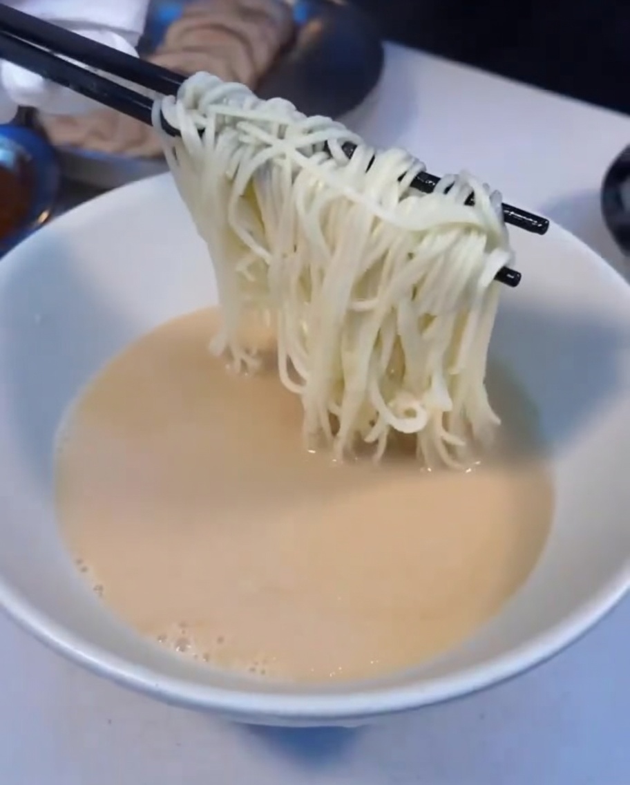 김이 모락모락 나는 라멘 면을 국물이 담긴 그릇으로 옮기는 모습.