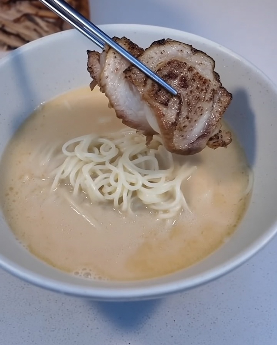 핀셋으로 구운 차슈 한 조각을 라멘 위에 올리는 모습.