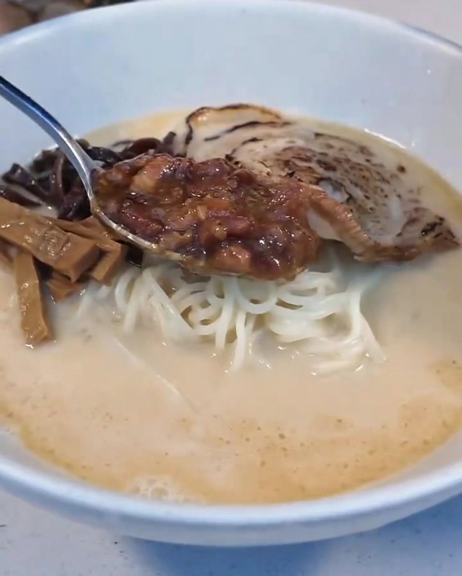 반숙란 옆에 풍미 깊은 조림 고기 소스를 한 숟가락 올리는 모습.