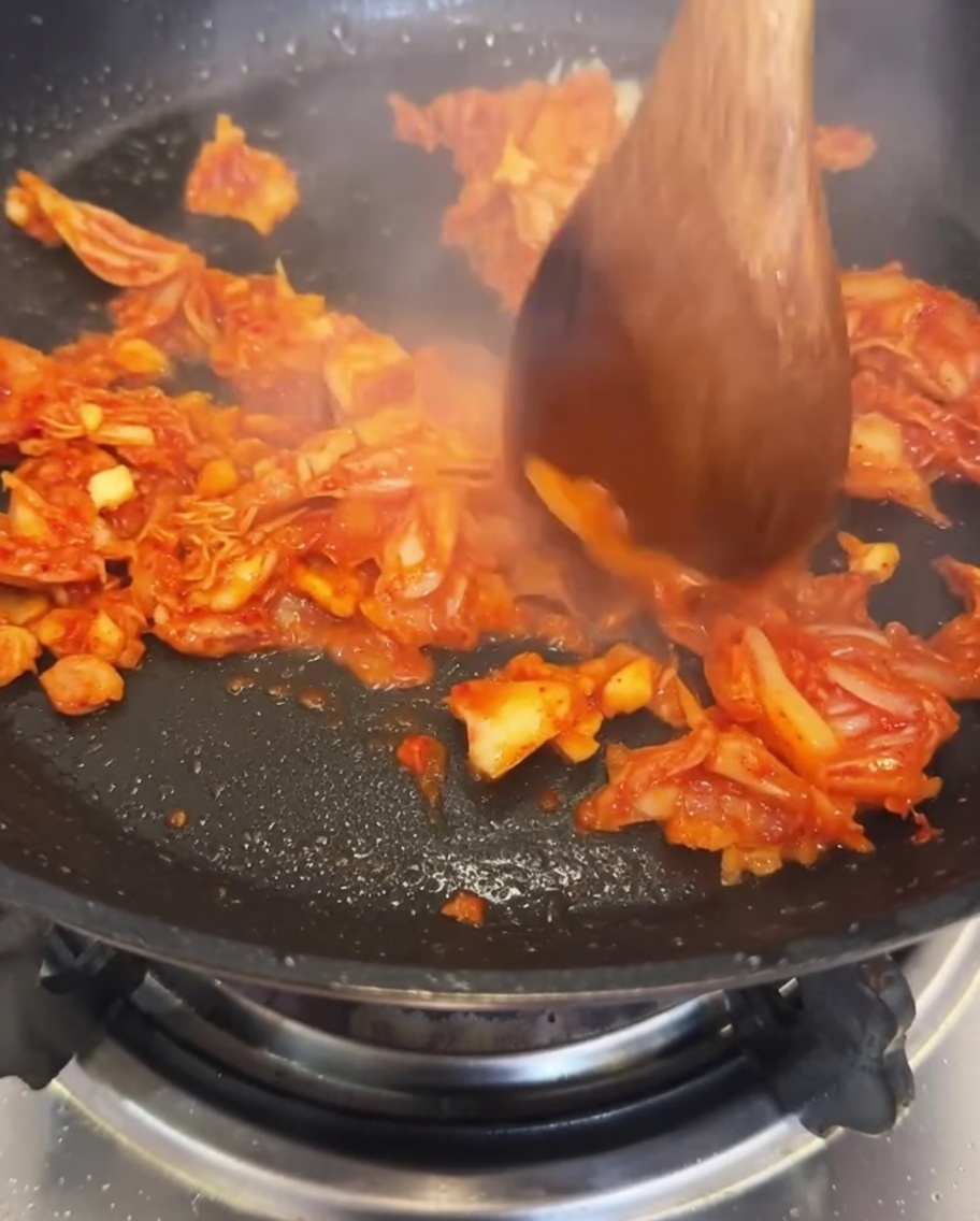 마늘과 김치를 볶은 팬에 물을 붓는 모습.
