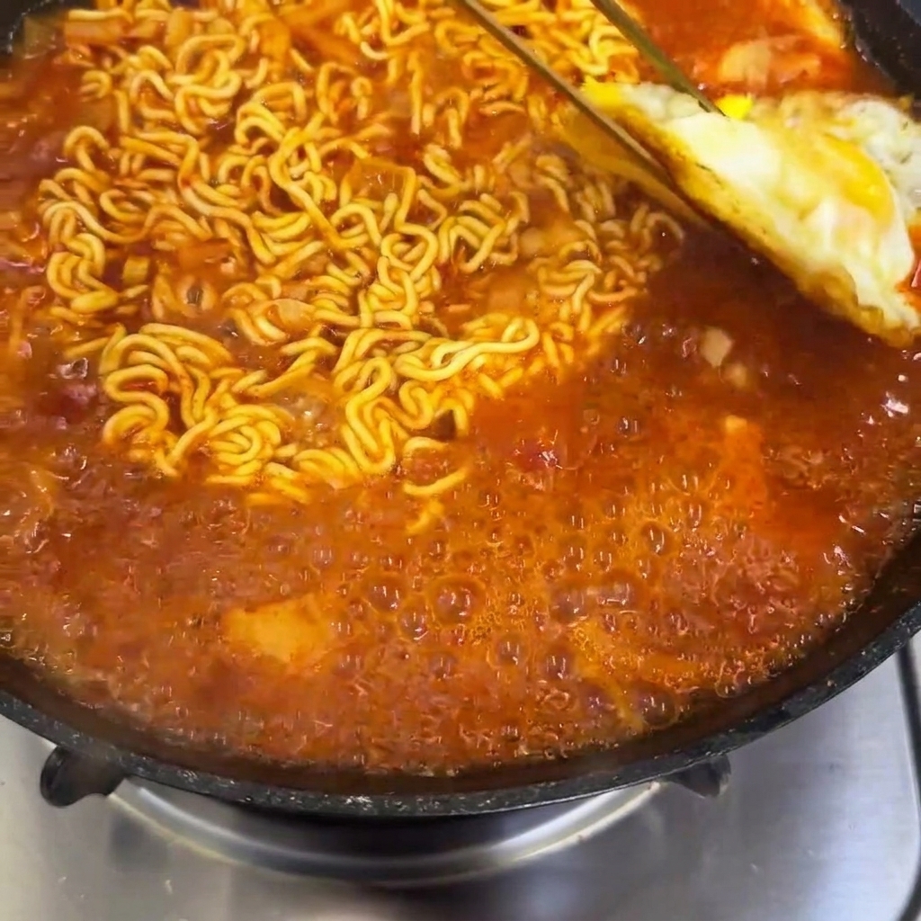 보글보글 끓고 있는 매운 라면 위에 미리 부쳐둔 계란 프라이를 올리는 모습.