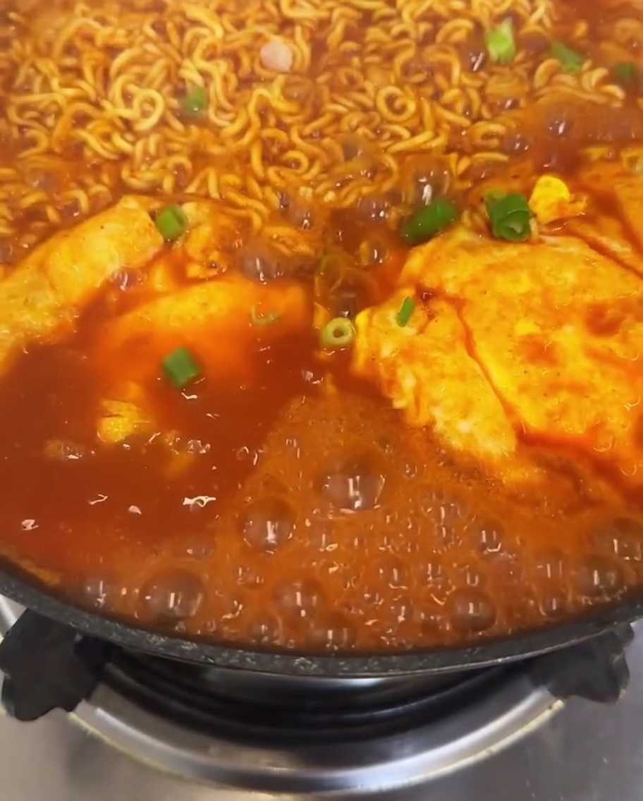 갓 썬 대파와 선명한 붉은 고추가 듬뿍 올라간 김치 라면 냄비 주변으로 국물이 보글보글 끓고 있는 클로즈업 뷰.
