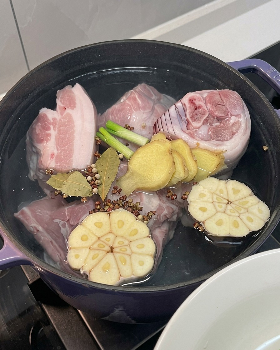 냄비 속 고기 위로 양파, 마늘, 생강, 대파와 각종 향신료를 넣는 모습.