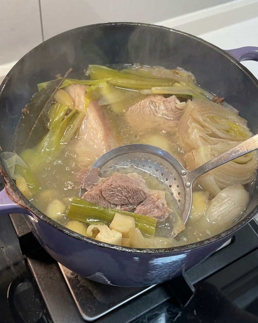 푹 삶아진 양파, 마늘, 생강 등의 채소를 육수에서 건져내는 모습.