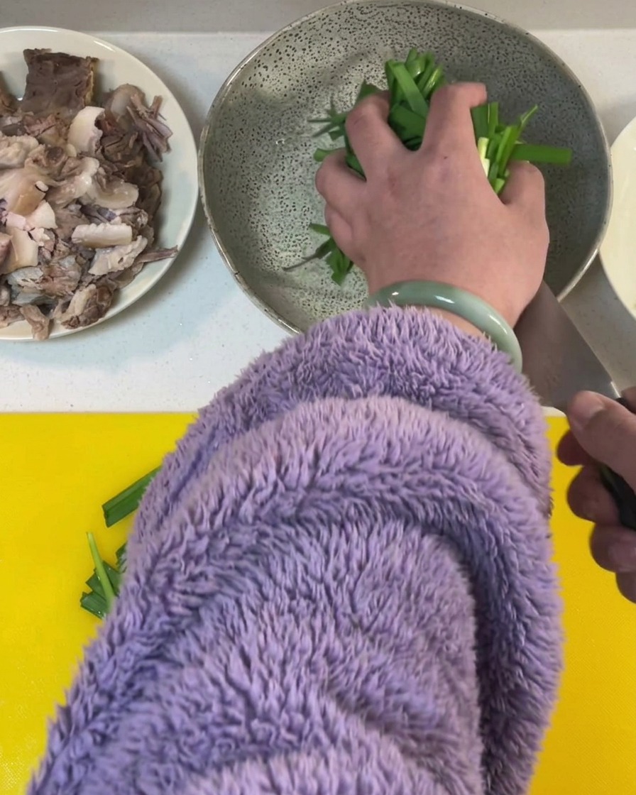 노란색 도마 위에서 신선한 부추를 일정한 크기로 써는 모습.