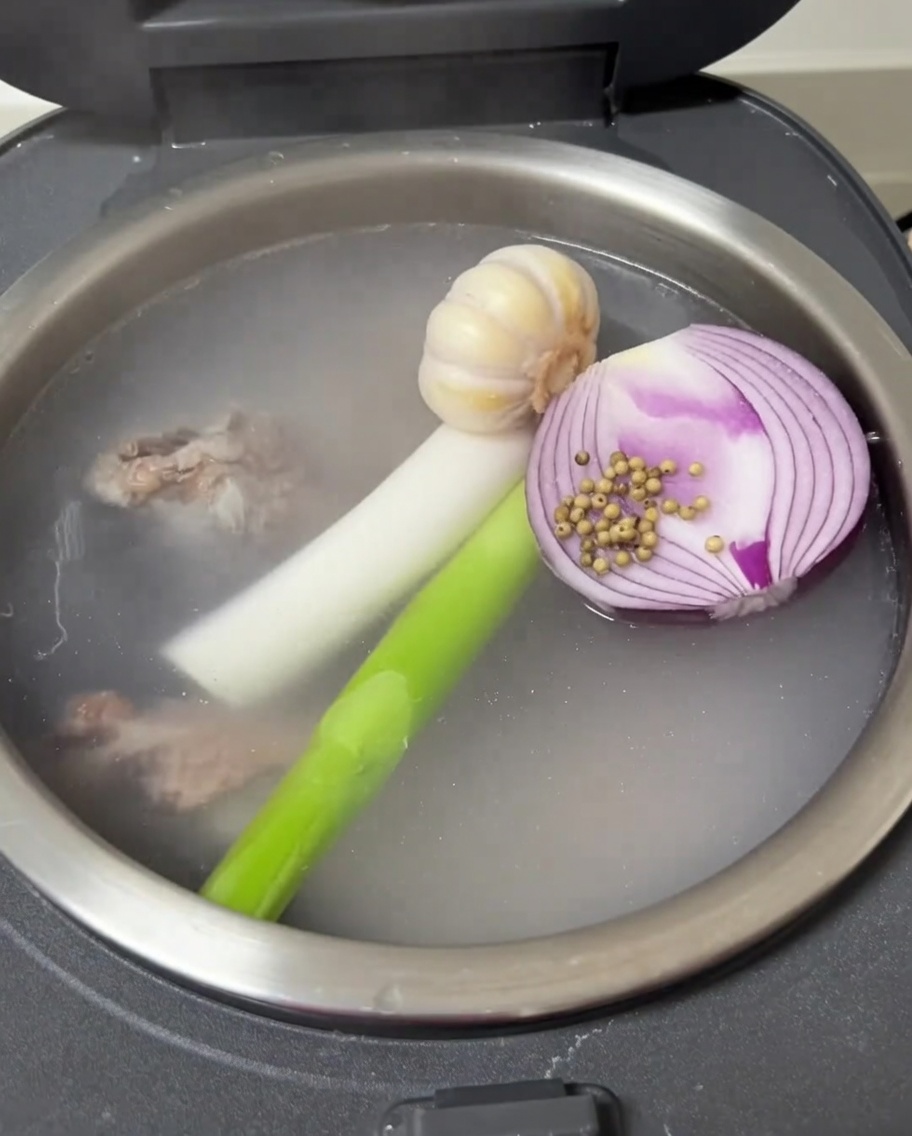 밥솥 안에서 마늘, 양파, 대파, 백후추와 함께 끓는 돼지 등뼈.