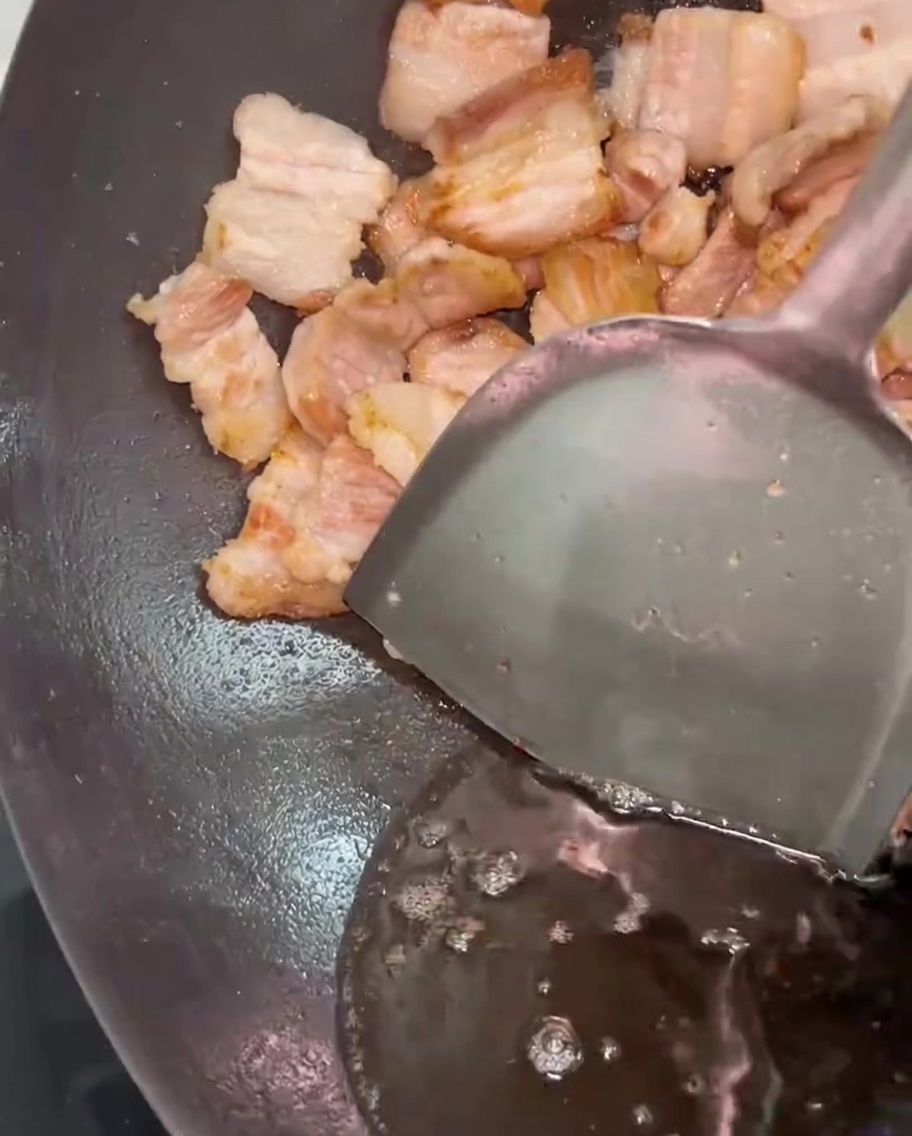 주걱으로 고기를 한쪽으로 밀고 여분의 기름을 덜어내는 모습.