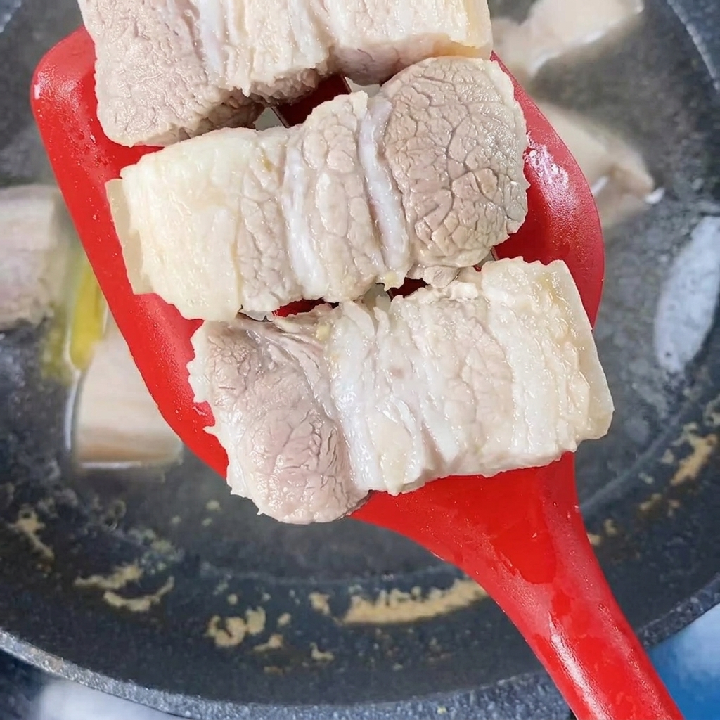 빨간색 조리용 주걱으로 끓는 물에서 데친 돼지고기를 건져내는 모습.