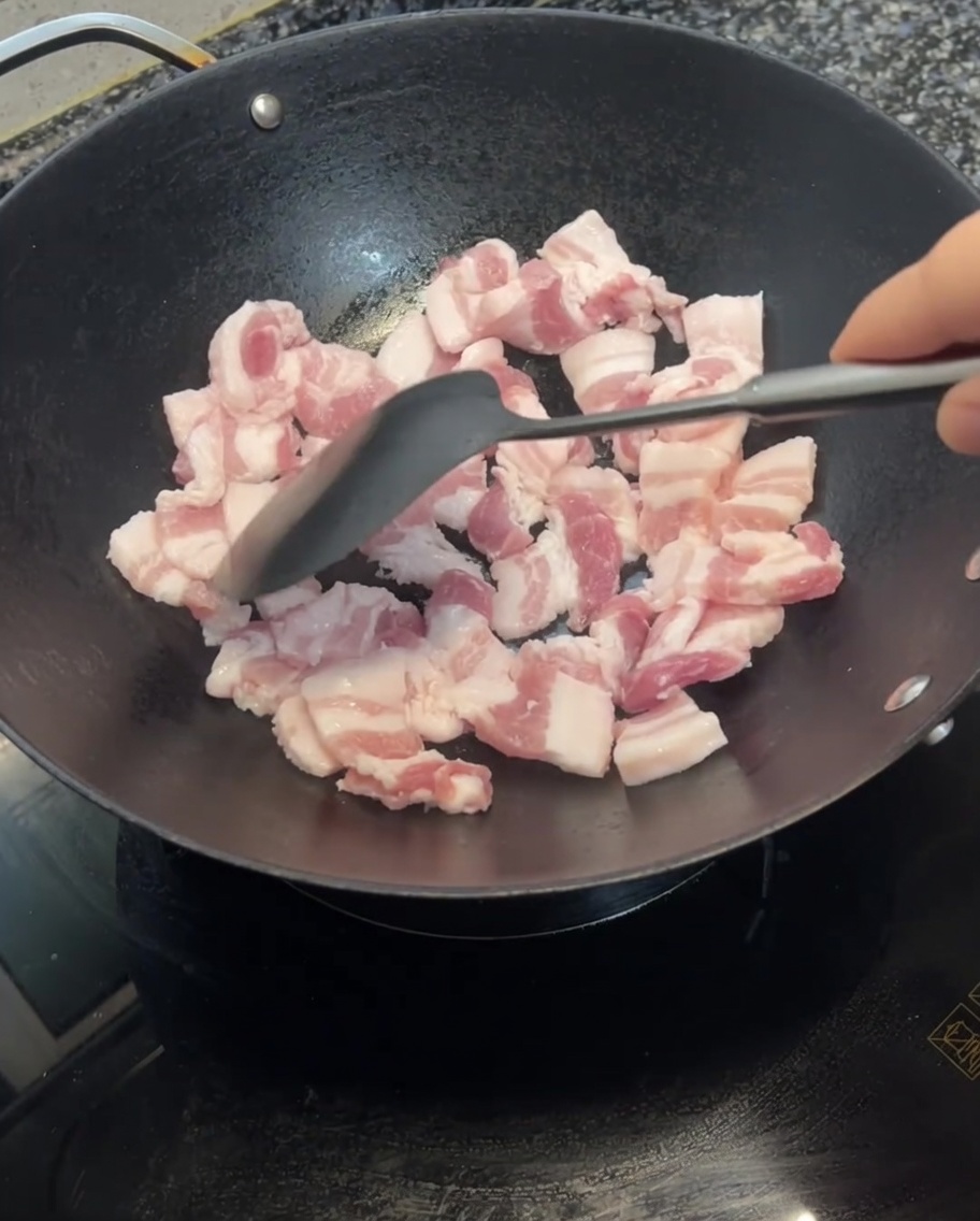 웍에서 삼겹살을 뒤집개로 볶으며 노릇하게 익어가는 모습.