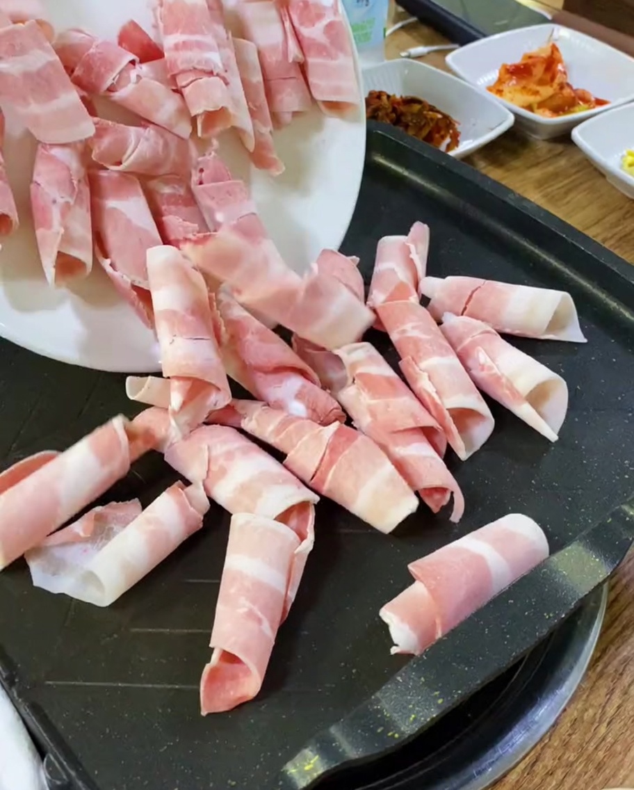 뜨거운 철판 위에 생삼겹살 슬라이스를 올리는 모습.