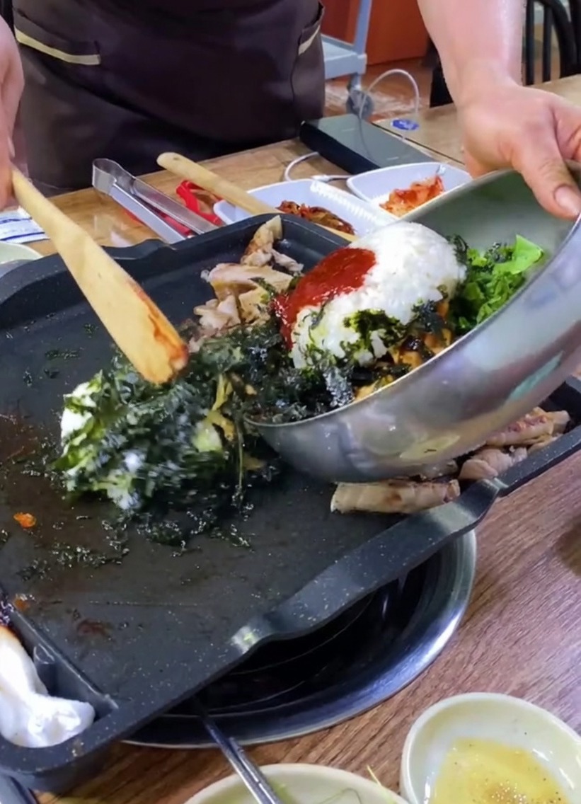철판 위 삼겹살 옆으로 김가루, 달걀, 채소가 섞인 밥을 붓는 모습.