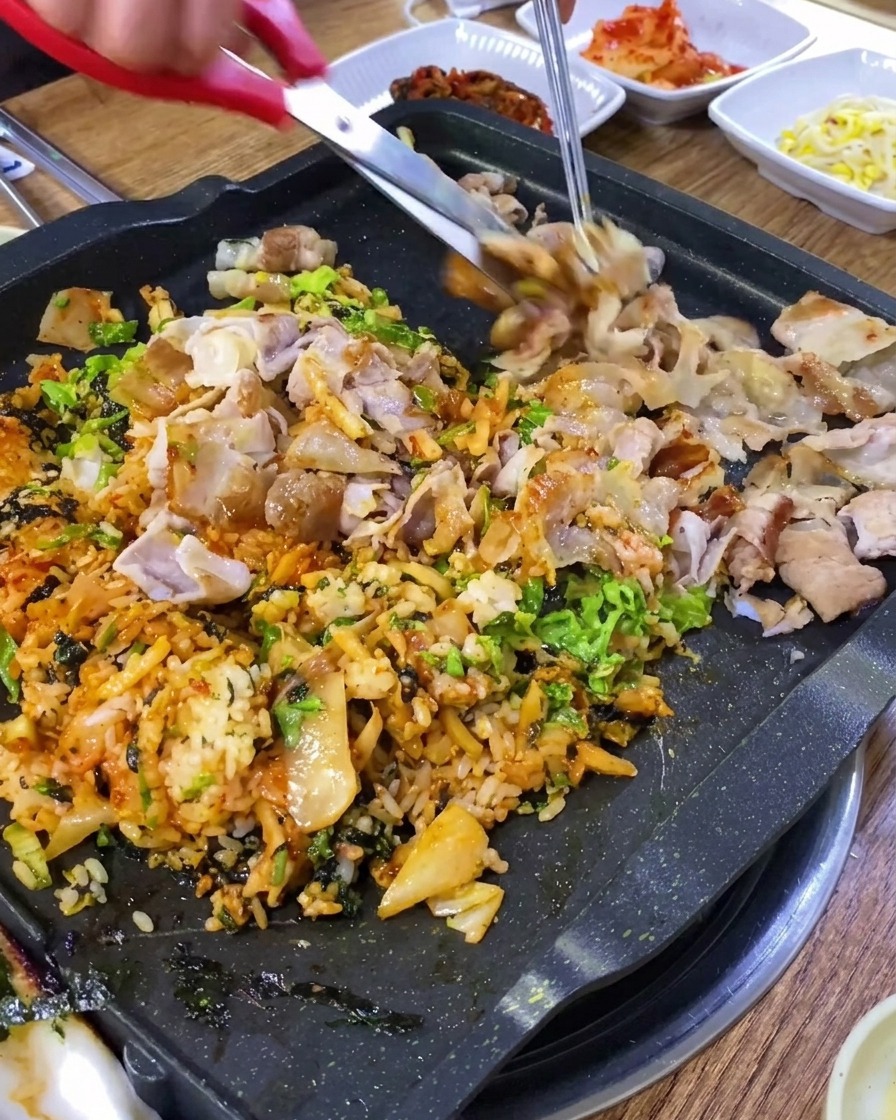 주방 가위로 철판 위에서 삼겹살을 작게 자르는 모습.