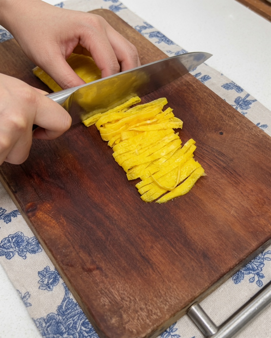 도마 위에서 달걀 지단을 칼로 가늘게 채 써는 모습.