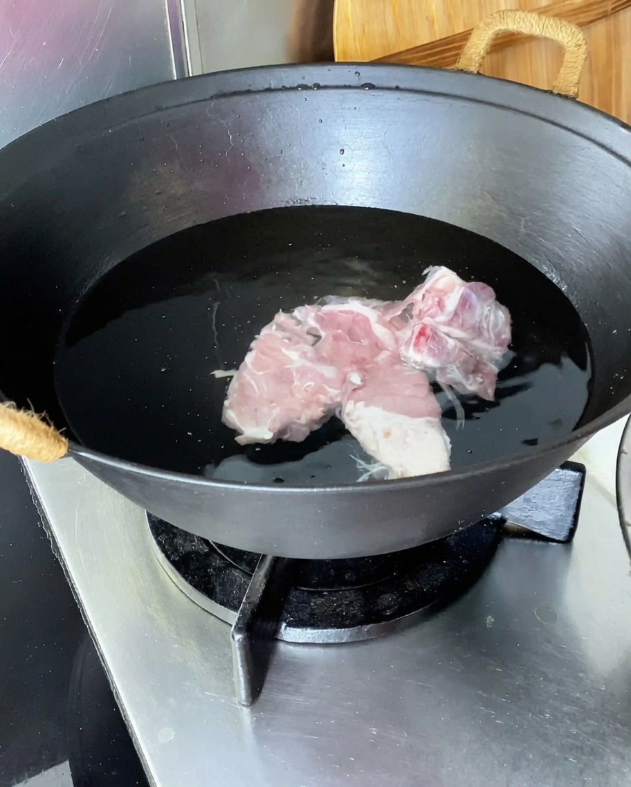 찬물이 담긴 웍에 생강, 대파, 맛술과 함께 담긴 돼지등뼈.