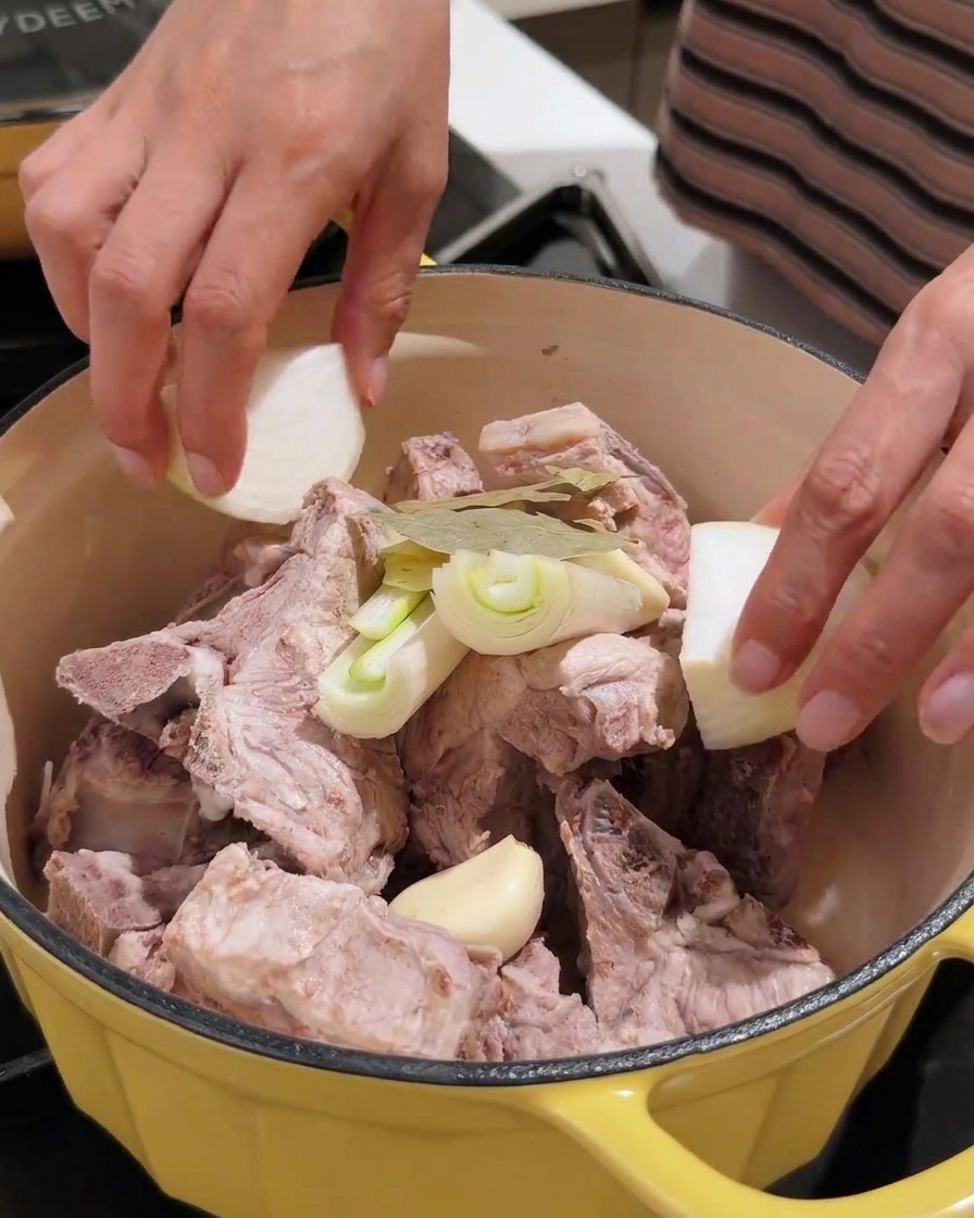 손질한 마늘, 양파, 된장 등의 향신료를 고기가 담긴 냄비에 넣는 모습