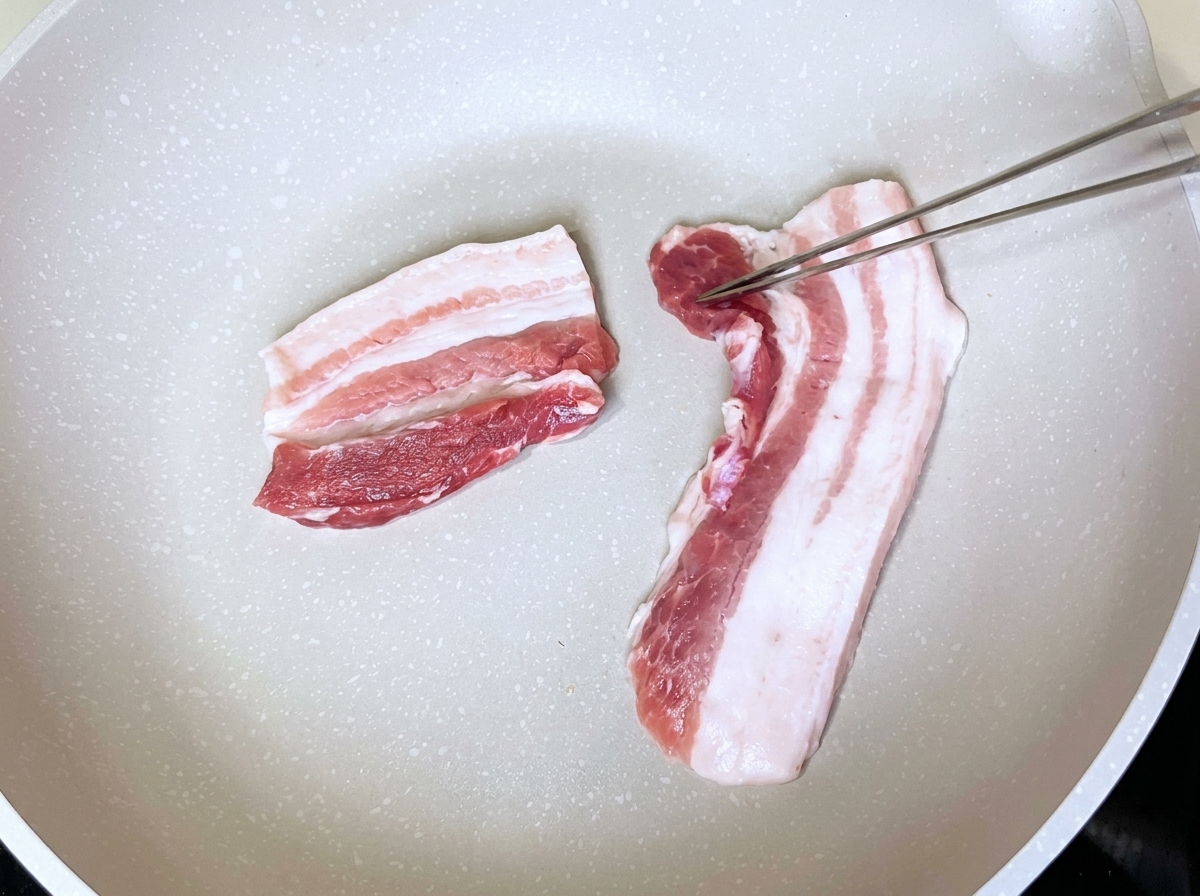마른 팬에 삼겹살을 올리고 집게로 뒤집는 모습
