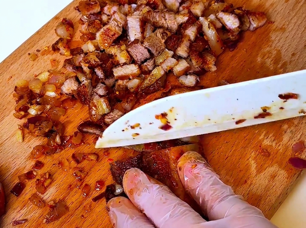 도마 위에서 익힌 고기와 양파를 칼로 잘게 다지는 모습