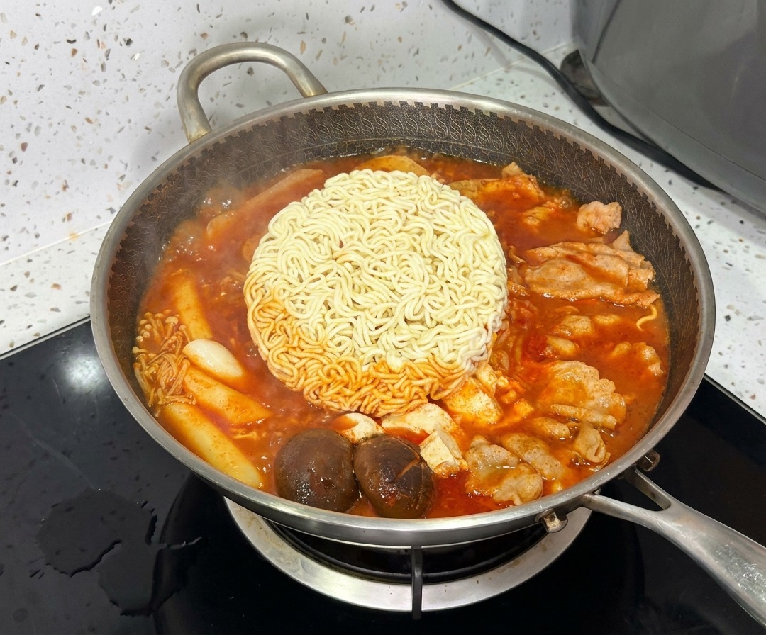 생동감 넘치게 보글보글 끓는 부대찌개 중앙에서 라면 면발이 익어가고 있는 모습.