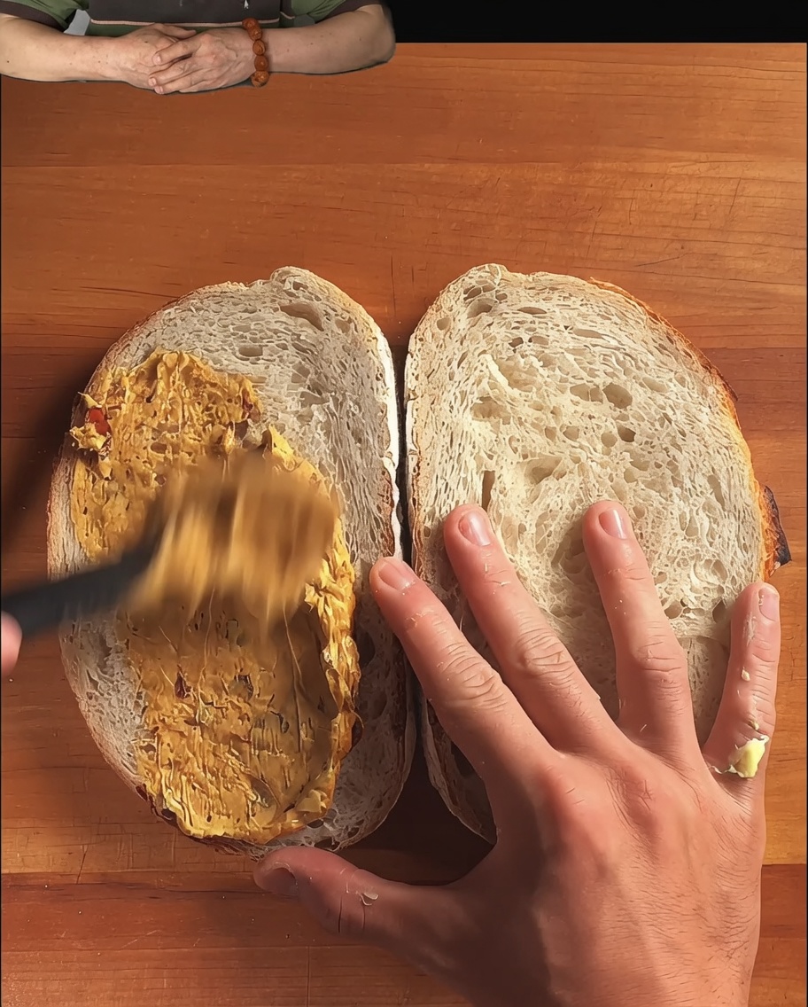 스푼으로 풍부한 소스를 부드럽게 펴 바르고 있는 러틱 사워도우 빵 조각들.